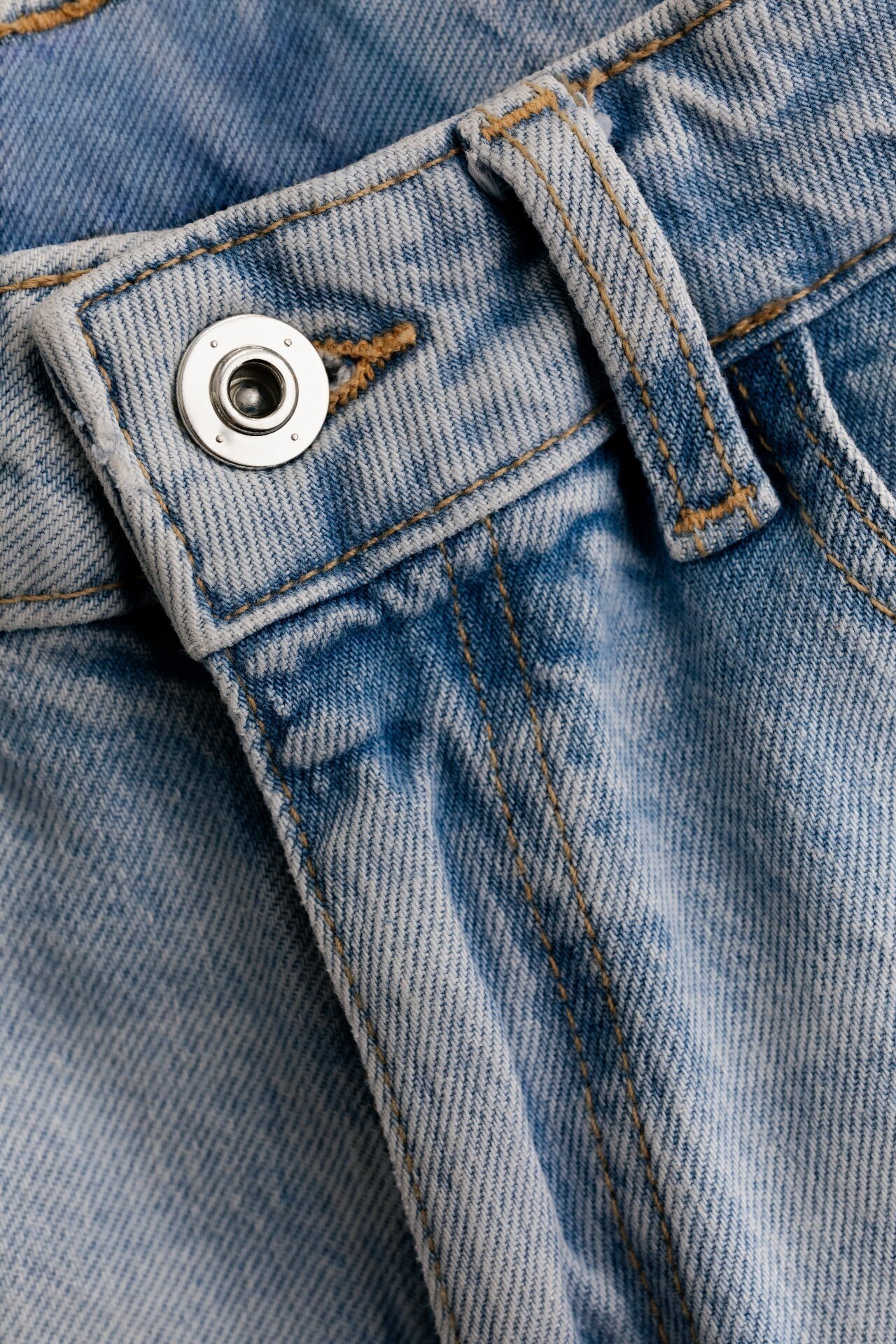 Light wash denim waistband detail with metal shank button and rivet