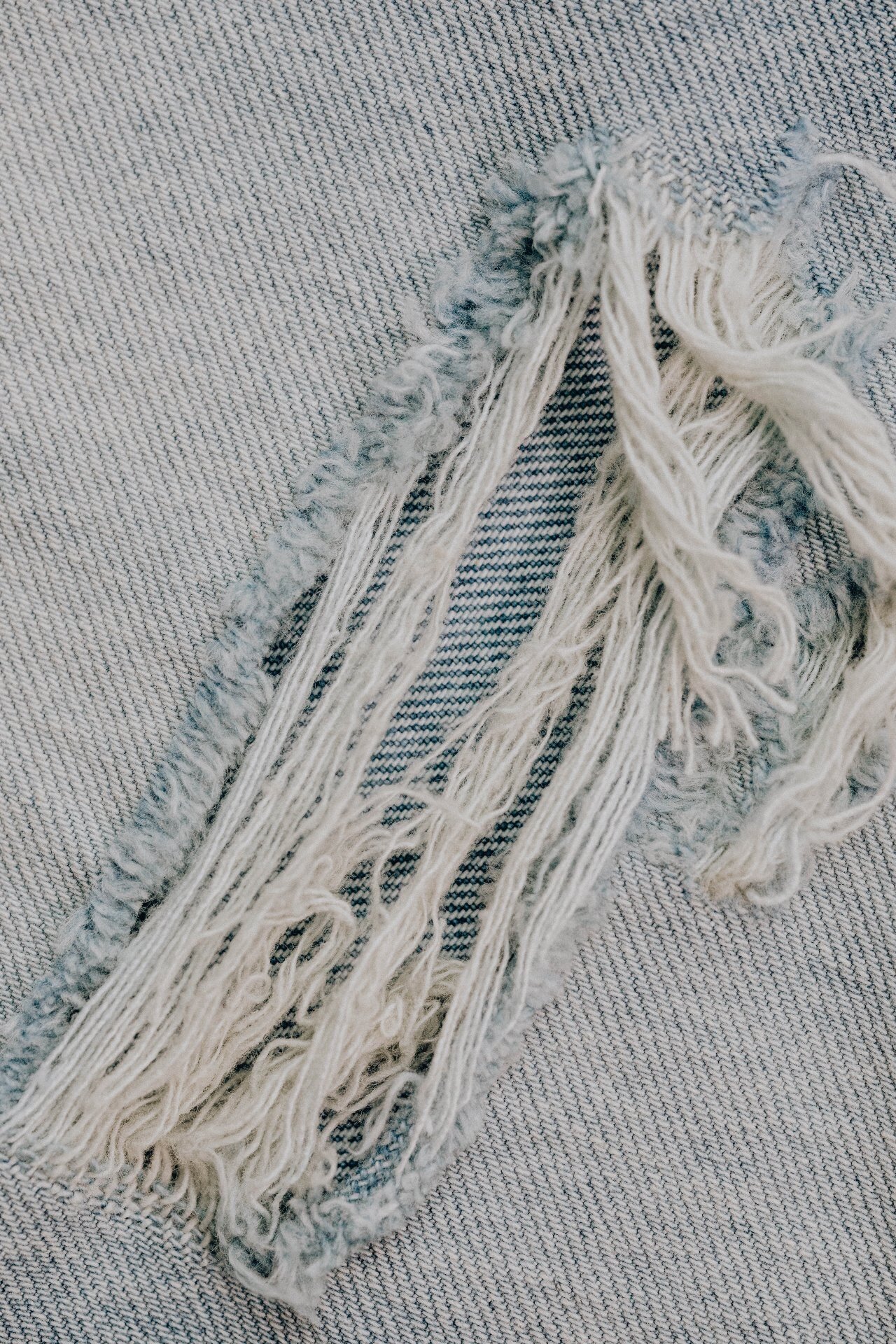 Raw edge denim fabric with frayed hem threads, distressed detail