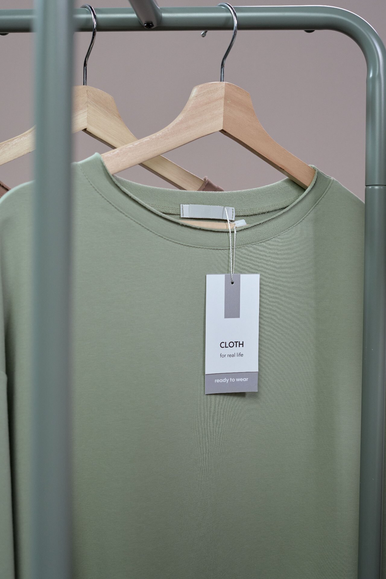 Sage green crewneck top on a wooden hanger with woven neck label and hang tag
