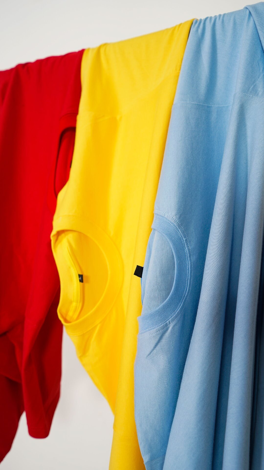 Three t-shirts in red, yellow and light blue showing custom garment dye colour range