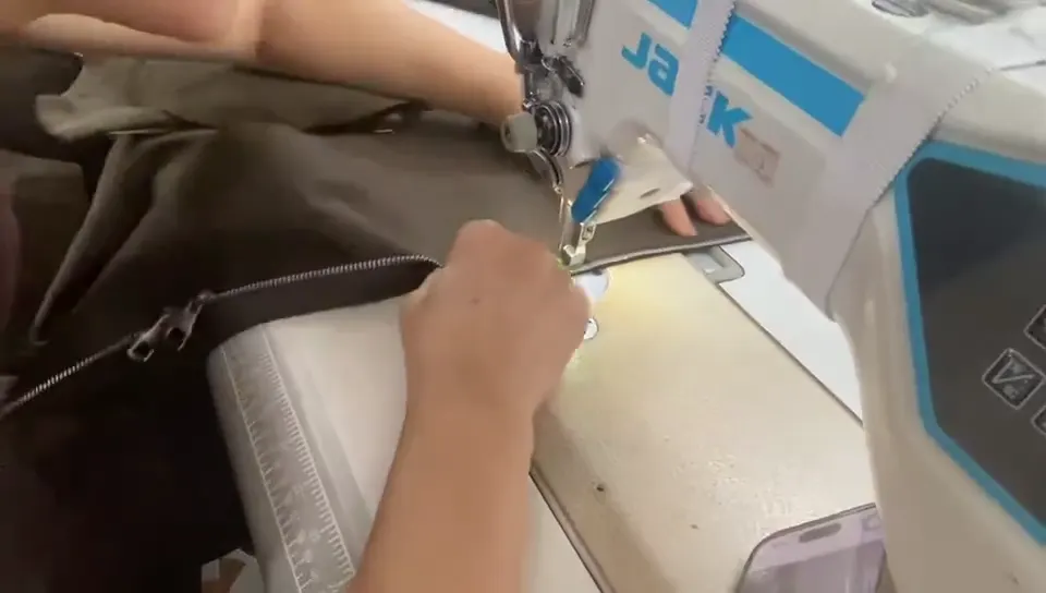 Hands guiding a zipper edge under an industrial sewing machine